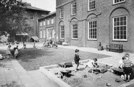 Black and white photo of children playing in the gardens and sandpit outside the Manor Gardens Welfare Trust building